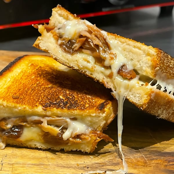 A grilled cheese sandwich, cut in half, with melted cheese and pastrami stretching between the halves.