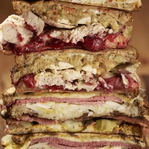 A towering stack of deli sandwiches, including turkey with cranberry, pastrami, and sauerkraut.