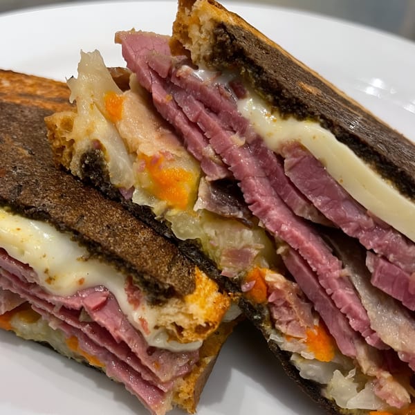 Close-up of a sliced Beantown Pastrami sandwich with pastrami, melted cheese, and sauerkraut.