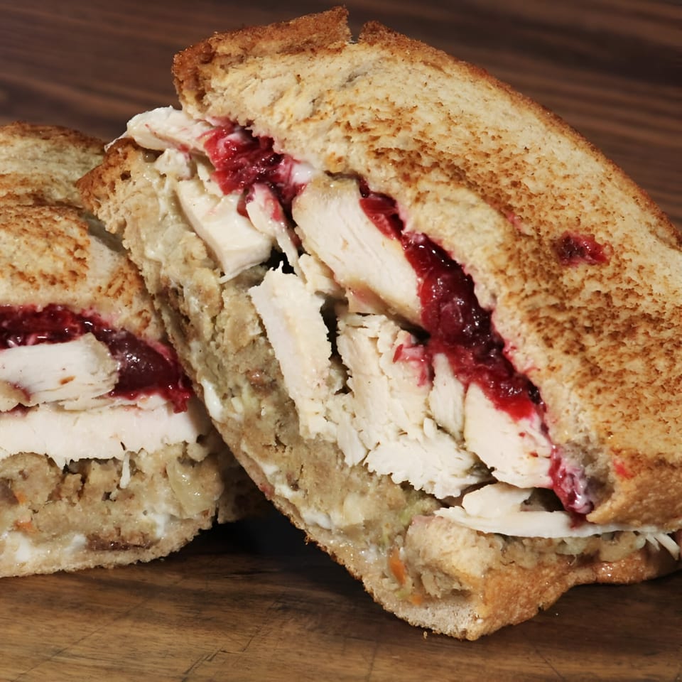 A Beantown Pastrami deli sandwich, cut in half, revealing turkey, stuffing, and cranberry sauce.