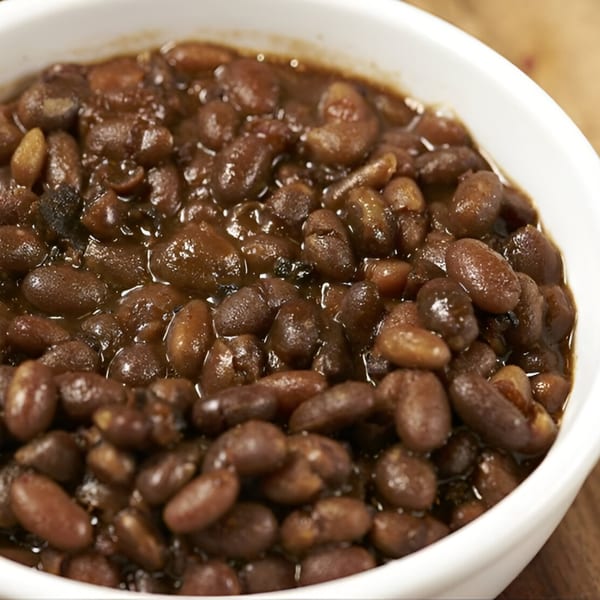 Close-up of a white bowl filled with dark brown baked beans in a rich sauce.