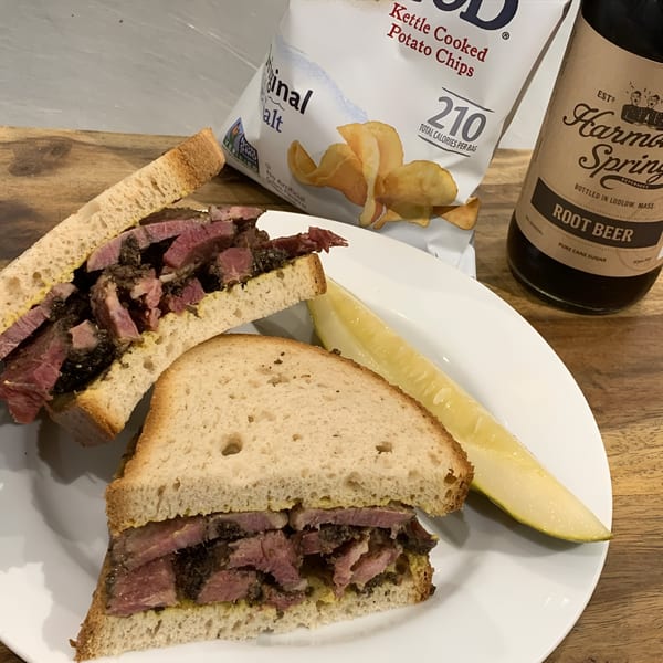 A Beantown Pastrami sandwich with a pickle, potato chips, and a bottle of root beer.